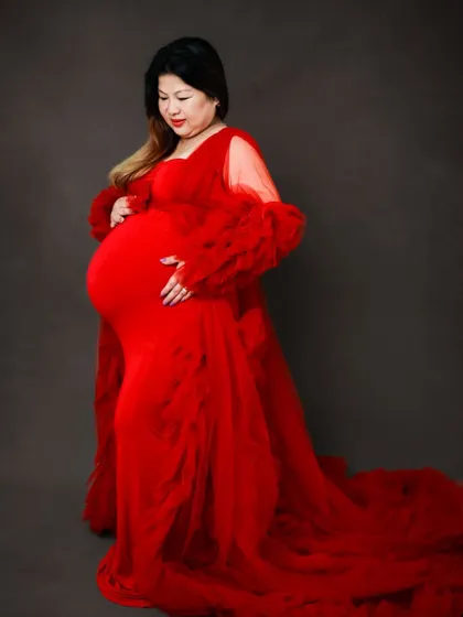 A classic portrait in a vibrant red ruffled gown against a simple dark background. The focus is on the mom-to-be and the stunning dress.