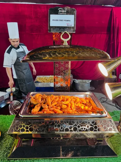 A chafing dish filled with golden fried prawns, kept warm under heat lamps.