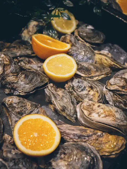 A bed of fresh oysters on ice with lemon and orange wedges.