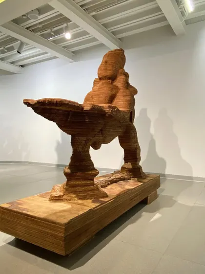 A monumental wooden sculpture by artist L.N. Tallur, displayed within a gallery at MAP. The high ceilings and neutral palette of the interior architecture provide a powerful backdrop for large-scale contemporary art.