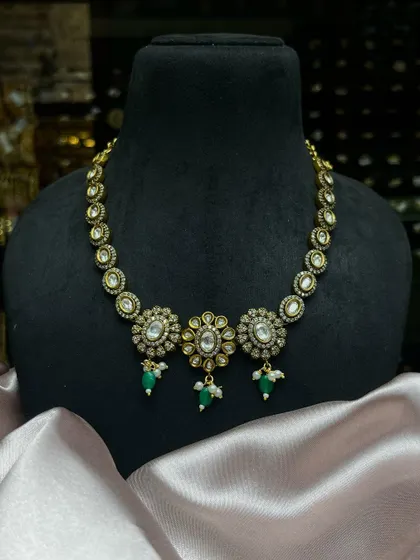 Adorn yourself with this exquisite Kundan necklace. The piece features three floral motifs with green bead drops, perfect for a subtle traditional look.