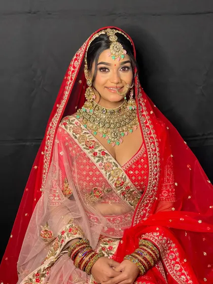 A smiling bride ready for her big day in a timeless red lehenga. The intricate floral embroidery adds a touch of softness to the bold color.