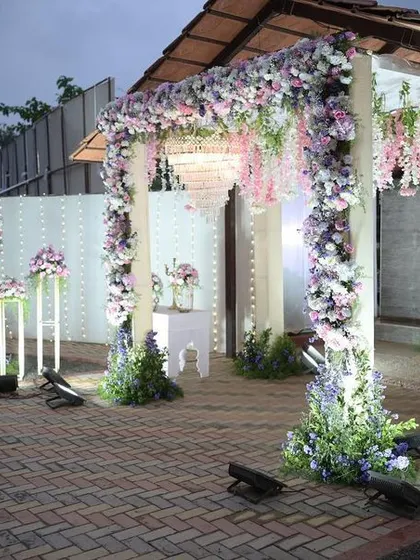 An elegant floral entrance for an evening reception, with arches of white and lavender flowers, soft lighting, and intricate white decor panels.