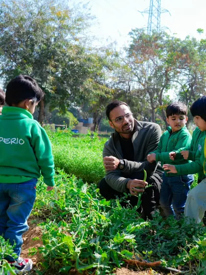 An instructor kneeling down to show a group of curious students a plant in the vegetable patch.