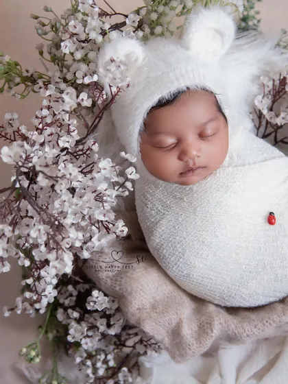 Wrapped in a pure white swaddle with a tiny ladybug friend. The contrast of the red ladybug on the white flowers and wrap is a simple but beautiful detail.