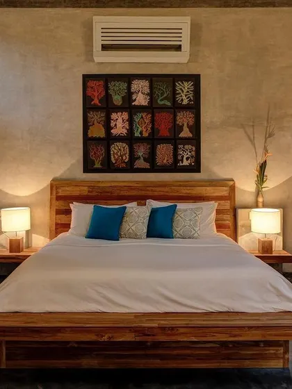 The bedroom of the private villa at Jalakara, featuring a custom wooden bed and artwork, with louvered shutters for privacy and ventilation.