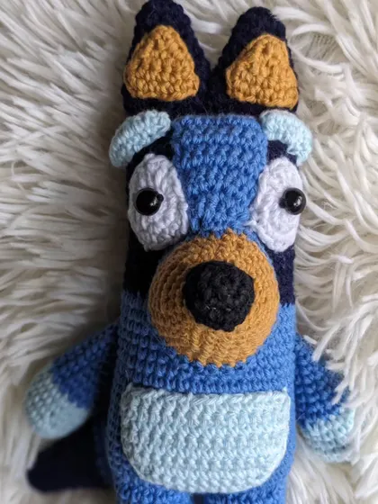 The Bluey crochet toy sitting on a soft, fluffy white surface.