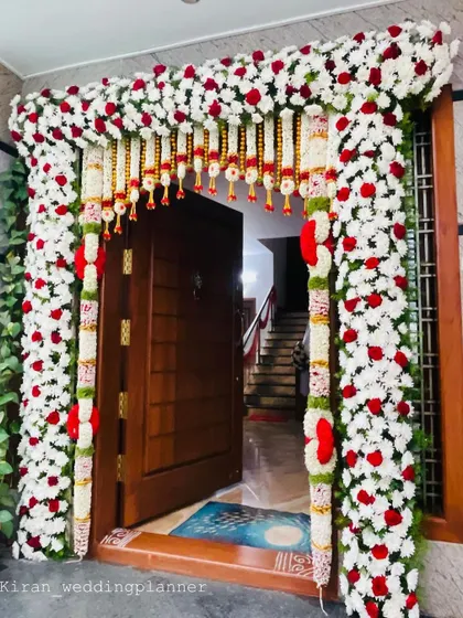 A beautiful floral door decoration for a home, using a thick frame of white chrysanthemums, red roses, and traditional hangings.
