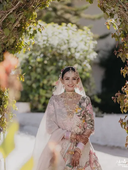 The bride, Sanskaara, smiling brightly as she walks through a sunlit archway of flowers, a perfect picture of bridal joy.