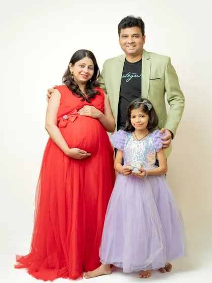 A full family portrait with the daughter holding tiny baby shoes. Everyone is dressed in celebratory colors, creating a bright and joyful family photo.