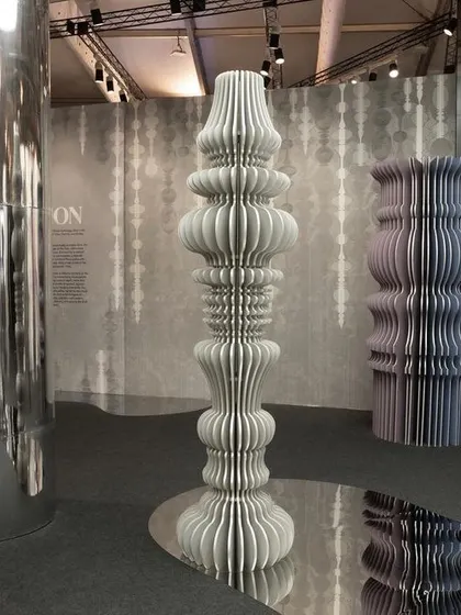 Sculptural totems made from layered, cut paper for the 'Silver Escapade' installation. These forms stand on a mirrored floor, creating infinite reflections and a dream-like, illusory dimension.