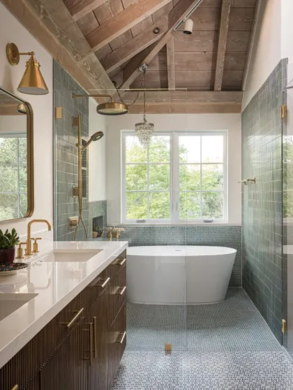 The master bathroom in the Saratoga home is a spa-like retreat. It features a freestanding tub, a spacious walk-in shower with green tiles, and a double vanity with brass fixtures. The exposed wood ceiling continues into this space, adding warmth and texture.