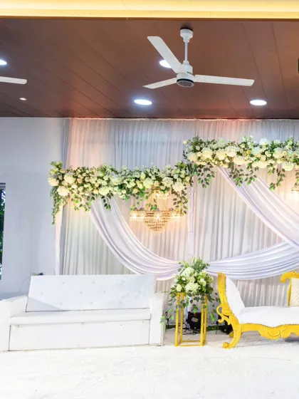 A wider view of the elegant all-white stage, showing the balance and symmetry of the floral arrangements and drapery that created a serene and beautiful backdrop.