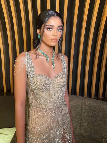 A modern reception look with a beaded gown and emerald jewelry. The makeup is soft and glamorous, with a focus on a subtle smokey eye and glowing skin.