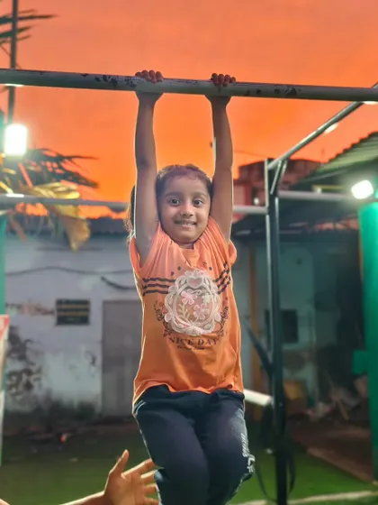 A young girl smiling while practicing her dead hang. This simple exercise is crucial for building grip strength for pull-ups.