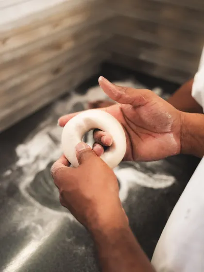 A baker holds a perfectly shaped ring of bagel dough. This is the first step in a two-part cooking process that makes our bagels authentic.
