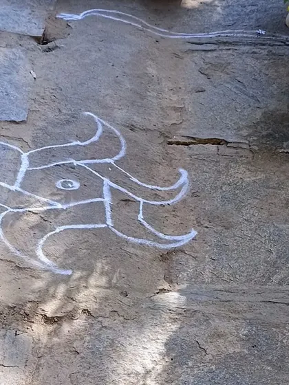 A simple and traditional chalk rangoli design drawn on the stone floor.