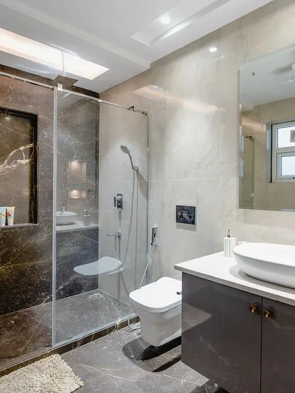 This view showcases the shower area, which features a stunning dark marble accent wall. The glass partition keeps the space feeling open and spacious.