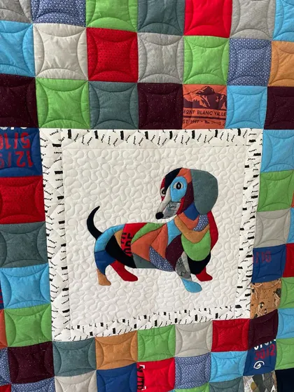 A close-up of the custom dachshund appliqué on a T-shirt memory quilt, showing the intricate stitching and fabric collage work.