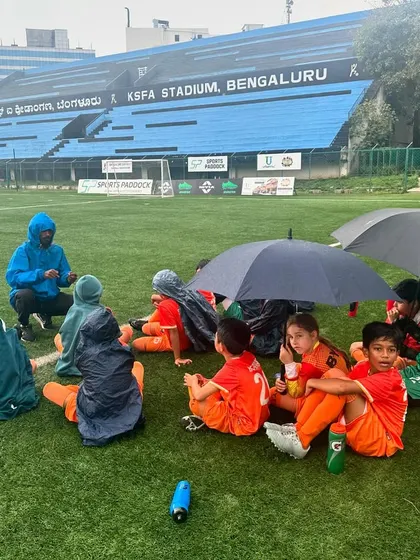 A coach gives a team talk in the rain, keeping the players focused despite the weather.