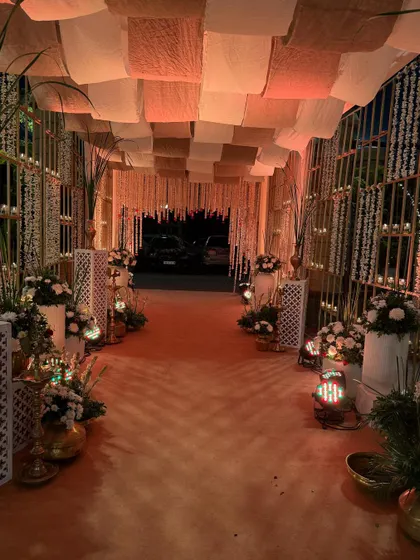 A warm and inviting entrance for an evening event. The aisle is lined with candles and floral arrangements, while the ceiling features a rustic fabric canopy, creating a cozy and intimate atmosphere.