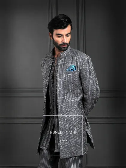 A charcoal grey kurta, woven with geometric lines and subtle shimmer. Finished with looped fabric buttons and a regal mandarin collar, it is a harmony of structure and elegance.