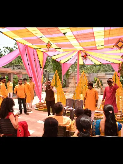 A wide shot of me addressing the guests at a Haldi ceremony, with the vibrant decor in the background.