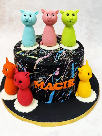 We play with color and art in this modern cat-themed cake. A dramatic black cake with neon paint splatters serves as the canvas for a parade of colorful, stylized cat figures, making it a unique and artistic choice for a cat lover.