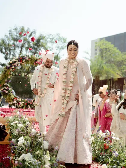 The couple walks down an aisle covered in rose petals, a perfect picture of happiness on their wedding day. The candid nature of the shot captures their genuine smiles.