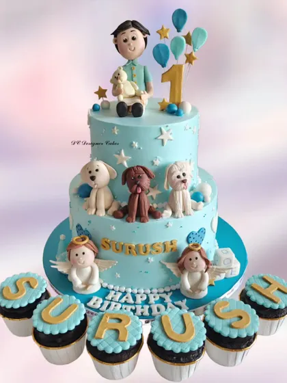 A truly personalized two-tier cake for a 1st birthday celebration. This design features the birthday boy with his beloved pets, angels, and matching cupcakes that spell out his name.