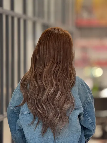 An ash blonde balayage on long hair, styled with loose waves to show off the beautiful color dimension. The denim jacket provides a great contrast to the cool tones in the hair.
