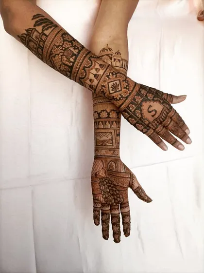A detailed shot of the arm portion of a bridal mehendi. You can see the different bands of patterns, including peacocks, elephants, and a personalized 'S' initial.