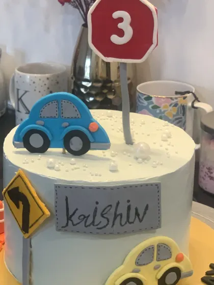 A cute car themed cake with fondant road signs. The design includes traffic cones, a stop sign, and little cars for a 3rd birthday.
