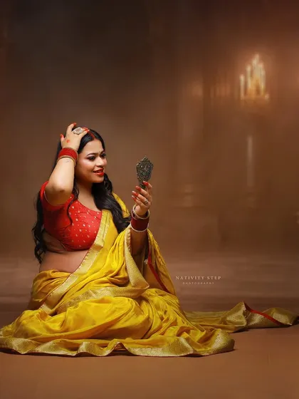 A moment of self-admiration, using a handheld mirror as a prop. The yellow saree and traditional jewelry complete this beautiful, culturally rich portrait.