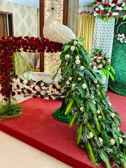 This is one of our signature creations, a magnificent peacock crafted entirely from fresh flowers and leaves. It stands beside a cradle adorned with red roses, making for a truly unique and artistic centerpiece for a naming ceremony or cradle ceremony.