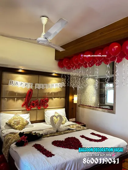 A simple yet beautiful birthday surprise setup in a hotel room. It includes a "Happy Birthday" banner, "love" foil balloon, and a bed decorated with rose petals and towel swans.