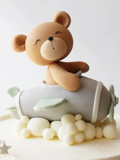 A cute teddy bear flying an airplane, a perfect topper for a little adventurer's cake.