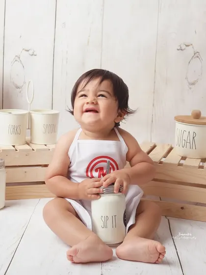 Our little chef is all smiles as he enjoys a jar of "milk." The rustic wooden props and vintage-style containers add to the charm of this delightful themed photoshoot.
