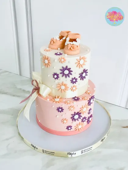 Welcoming a new little one with this adorable two-tiered baby shower cake. The design features delicate flowers and a pair of tiny, handcrafted baby booties on top.