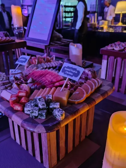 This checkerboard-patterned platter holds a variety of cheeses, including smoked English cheddar, alongside sliced oranges and strawberries. It's an example of how we use creative presentation to elevate our food displays.