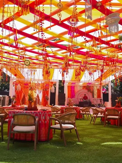 An overview of the guest seating area. The space is covered with a colorful canopy of red and yellow ribbons, with tables dressed in patterned cloths and rustic chairs, creating a cohesive and festive look.