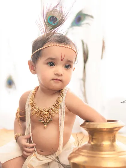 A simple yet powerful portrait. Against a clean, white background, the focus is entirely on the baby's innocent expression and the traditional Krishna styling.