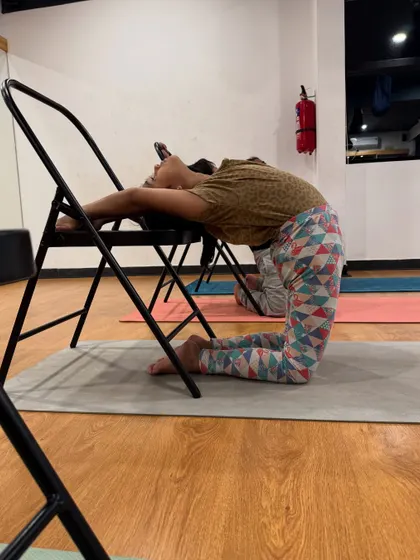 A supported camel pose using a chair. This modification allows for a deep backbend while ensuring the neck and spine are protected.