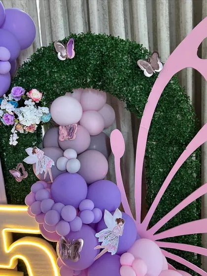 A detailed view of the fairy-themed decor, focusing on a large butterfly wing prop made of balloons and a faux-grass arch. This shot highlights the intricate combination of balloons, flowers, and fairy cutouts that create our enchanted forest look.