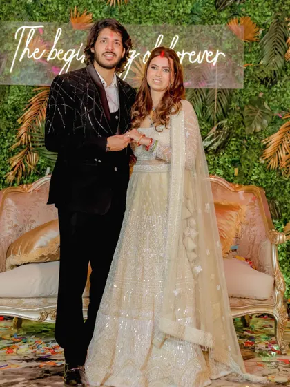 A happy portrait of the couple at their engagement, with a neon sign in the background reading 'The beginning of forever'.