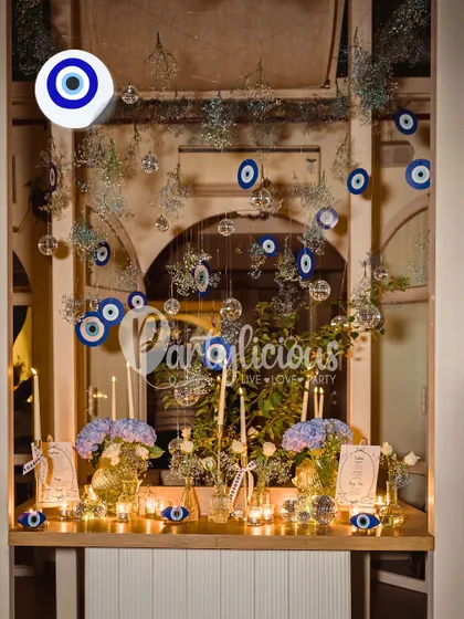 This whimsical setup features a cascade of hanging Evil Eye charms and delicate glass baubles. It creates a magical, protective canopy over the dining area, perfect for an intimate and meaningful celebration.