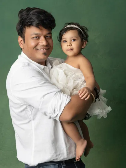 A proud father holds his daughter close. His smile and her sweet gaze towards the camera make for a heartwarming father-daughter portrait.
