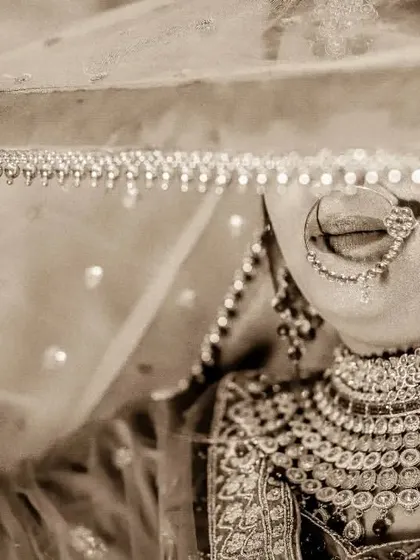 A sepia-toned bridal portrait with a vintage feel. The bride is lifting her veil, creating a sense of anticipation and revealing her beautiful details.
