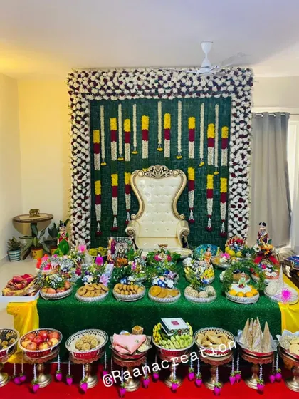 Even in a more intimate home setting, I can create a beautiful ceremonial space. This setup for a housewarming or small function features a backdrop of banana leaves and flowers, a ceremonial chair, and a full spread of decorative trays.