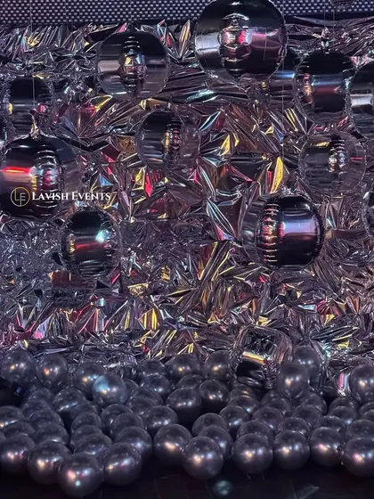 A unique and futuristic photobooth with a crumpled silver foil backdrop and metallic orbs.